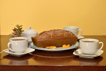 Brown table with two coffee cups, 2 sugar bowls and an orange cake on a plate.