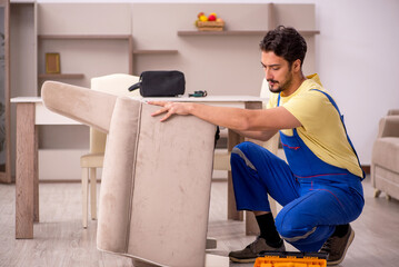 Young male carpenter repairing arm-chair at home