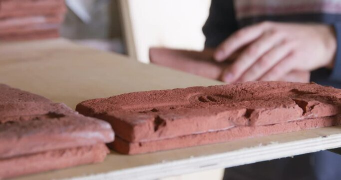 Person carefully puts tile based on casts of old bricks with stamp on shelf of the rack for final drying or for storage in warehouse, close up. Workflow in interior workshop