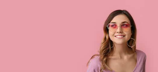 Pretty smiling young woman wearing stylish sunglasses on pink background with space for text