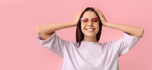 Happy young woman wearing stylish sunglasses on pink background