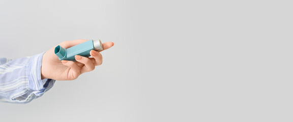 Female hand holding asthma inhaler on light background with space for text
