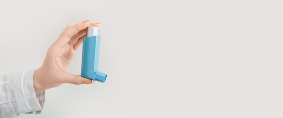 Female hand holding asthma inhaler on light background with space for text