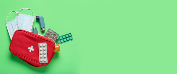 First aid kit with pills, inhalers and medical masks on green background with space for text