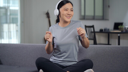 Fototapeta na wymiar Happy woman with headphones and listening to music sitting on sofa at home.