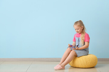Pretty girl sitting on pouf and playing with pop it fidget toys near color wall - obrazy, fototapety, plakaty