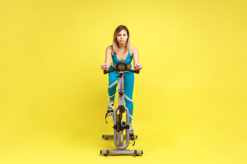 Attractive confident young woman riding on spinning bike, cycling on gym machine bicycle,...