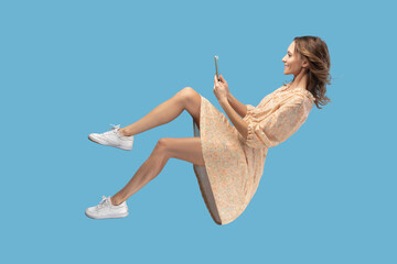 Hovering in air. Smiling girl in yellow dress levitating with mobile phone, reading message...