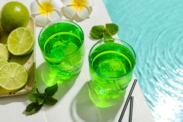 Glasses of fresh lime soda on edge of swimming pool, closeup