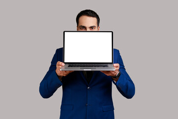 Bearded businessman covering half of face with laptop with empty display for advertisement or...