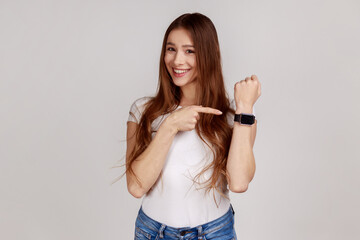 Portrait of positive cheerful woman showing wrist watch and looking happily at camera, reminding of...