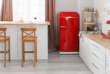 Interior of light kitchen with retro fridge, white counters and chairs