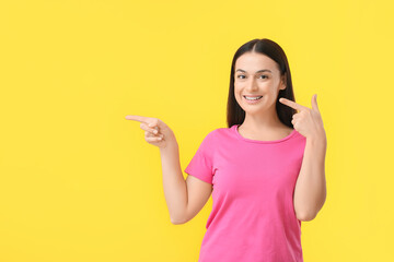 Beautiful woman with dental braces pointing at something on yellow background