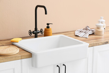 Fototapeta na wymiar Cleaning sponge and detergent near ceramic sink in kitchen