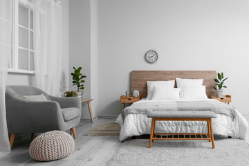 Interior of bedroom with comfortable bed and stylish clock on light wall