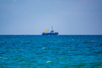 Fishing boat in blue sea and clear sky with birds flying overhead.