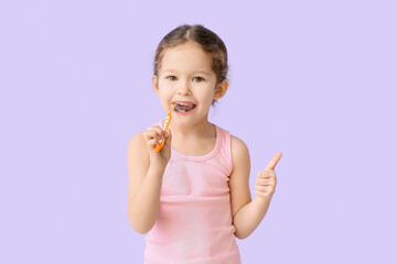 Adorable little girl brushing teeth on lilac background