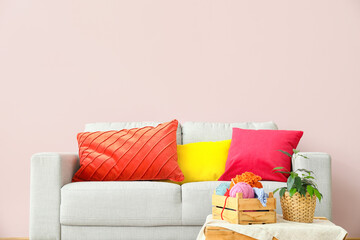 Modern sofa with pillows and houseplant on table near color wall in room