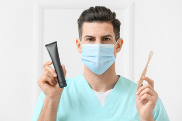 Male dentist with activated charcoal tooth paste and brush on light background