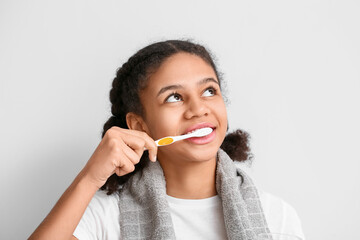 African-American teenage girl brushing teeth on light background