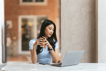 Portrait of Asian young female working on laptop and financial report at coffee shop.