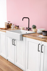 Counters with ceramic sink and kitchen utensils near pink wall