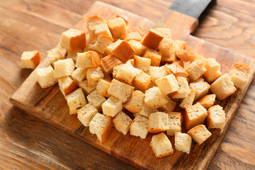 Chopping board with tasty croutons on wooden background, closeup