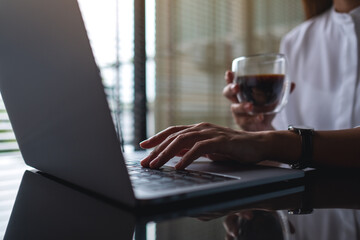 Closeup image of a business woman working on laptop computer while drinking coffee in office