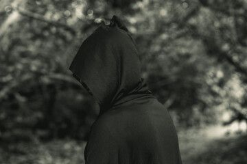 The black figure of a man in a black cloak stands in the forest. soft focus