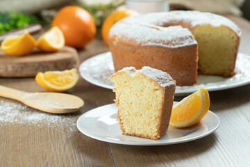 Close up piece of moist orange fruit cake on plate with orange slices on wooden table. Delicious...