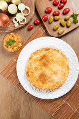 Chicken pie with cottage cheese, tomatoes, onion and olives on wooden table and white plate. Top view
