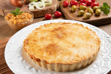 Chicken pie with cottage cheese, tomatoes, onion and olives on wooden table and white plate