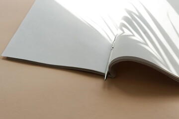 Open magazine mock up, pen  and palm leaf shadows on beige background. copy space