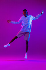Fototapeta na wymiar Full body portrait of ecstatic African man jumping in modern neon light studio background