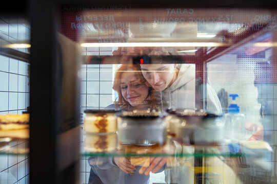 Photo of a young happy couple through the reflections of shop windows who choose dessert in a cafe