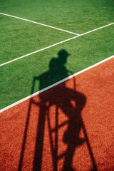 Tennis referee's shadow on a brand new outdoor tennis court. Vibrant green and brown with clear...