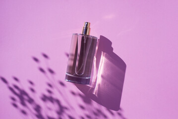 Transparent bottle of perfume on a lilac background. Fragrance presentation with daylight. Trending...