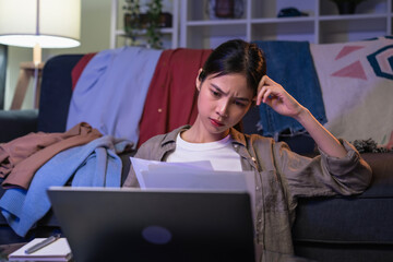 Unhappy young Asian woman hand holding expense bill and calculation about debt bills monthly at...