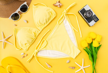 Top view of bikini and sunglasses with beach accessories on the yellow background. Summer time concept.