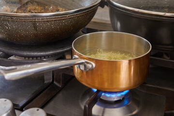 Saucepan with handle from copper and stainless steel on gas stove fire