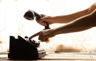 A woman's hand dials a phone number on an old phone at home on the table, a retro phone is black