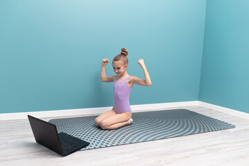 A young girl is doing gymnastics in front of a laptop. Classes at home
