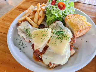 Close-up of pork steak topped with cheese garnished with fries, bread and salad.