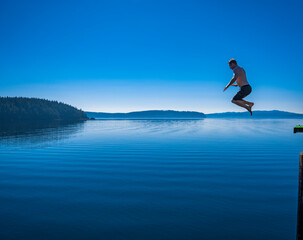 Adventurous athletic man jumping off a pier into a body of calm water.