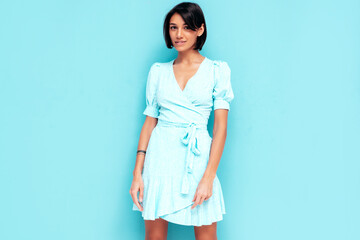 Portrait of young beautiful smiling female in trendy summer dress. Carefree woman posing near blue wall in studio. Positive model having fun indoors. Cheerful and happy. Isolated