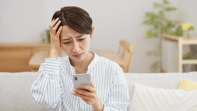 ソファーに座りながらスマートフォンを使う若い女性	
