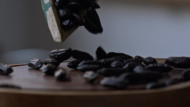Organically Grown South American Black Dried Tonka Beans Poured onto Wood Chopping Board in Slow Motion, Closeup