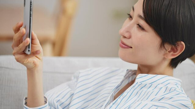 ソファーに座りながらスマートフォンを使う若い女性	
