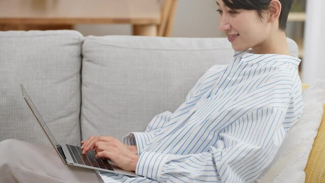 ソファーに座りながらパソコンを使う若い女性	
