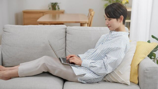 ソファーに座りながらパソコンを使う若い女性	
